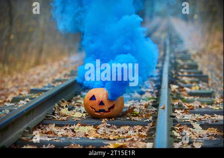 Lächelnder halloween-Kürbis mit hellblauem Rauch auf den Schienen im Wald Stockfoto