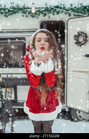 Die junge Frau im weihnachtsmann-Kostüm ziert den Weihnachtsbaum auf dem Wintercampingplatz und bereitet sich auf das neue Jahr vor. Konzept zur Feier des neuen Jahres Stockfoto