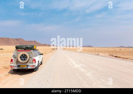 Pickup Truck fährt auf einer langen, geraden Wüstenstraße in Richtung Berge. Stockfoto