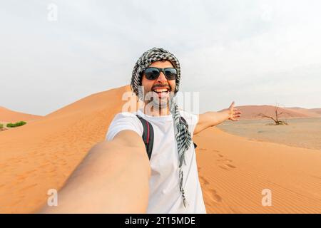 Glücklicher Mann Tramp in Sonnenbrille nimmt ein Selfie-Foto in Die Wüste vor dem Hintergrund einer Düne aus Weiß Sand Stockfoto