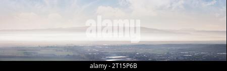 Panorama einer Landschaft mit ländlichen Feldern am Fuße einer Bergkette im Morgennebel. hunedoara-Tal in rumänien im Herbst Stockfoto