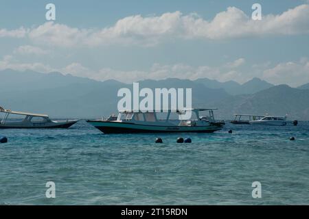 Ein einsames Boot treibt auf Gili Trawangans kristallklarem Wasser. Majestätische Berge und schimmernde Wolken zieren den azurblauen Himmel. Stockfoto