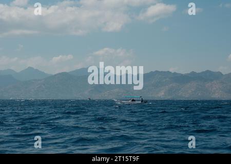 Ein einziges Boot segelt durch die endlose Weite des offenen Meeres von Gili Trawangan. Das weite, azurblaue Wasser reicht bis zum Horizont, mit dem Geist des Abenteuers. Stockfoto