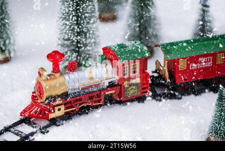 Spielzeuglokomotive im Schnee mit Weihnachtsbaum. Weihnachten und Neujahr Hintergrund. Kreative Winterweihnachtskomposition mit Zug. Stockfoto