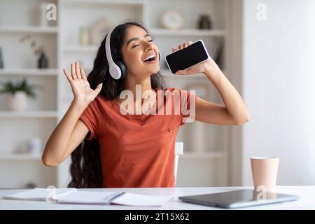 Positive junge Frau, die ein Headset trägt und Musik hört und singt Stockfoto