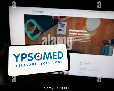 Person mit Smartphone mit Logo des Schweizer Medizintechnikunternehmen Ypsomed Holding AG vor der Website. Schwerpunkt auf dem Display des Telefons. Stockfoto