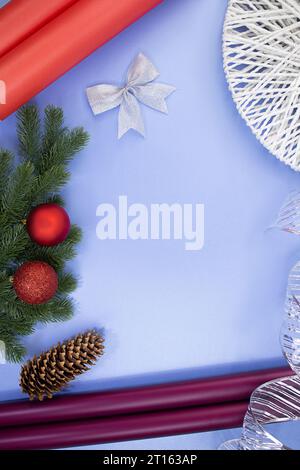 Geschenkrollen aus Papier, Kiefernkegel, Schleife und Band, Tannenzweige mit Weihnachtskugeln auf blauem Hintergrund. Neujahr Weihnachten. Zubehör für Geschenkverpackung Stockfoto