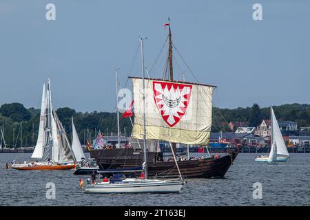 Kiel, Schleswig-Holstein, Deutschland. Juni 2023. Die Hanse Kogge von Kiel (Mitte hinten), ein originaler Nachbau eines mittelalterlichen Zahnradschiffs aus dem Jahr 1380, nimmt an der Windjammerparade in der Bucht Kieler Förde in der Ostsee mit etwa 60 großen Schiffen, traditionellen Segelschiffen, Dampfschiffe und Hunderte von Segelyachten im Rahmen der Kieler Woche, einer jährlichen Segelveranstaltung in Kiel. Stockfoto