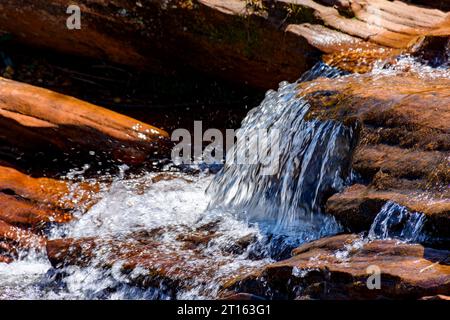 Wasser fließt über die Felsen und bildet einen kleinen Wasserfall aus klarem, transparentem Wasser Stockfoto