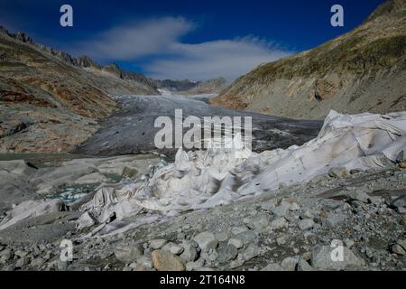 Klima | Albedo | Rhone: Riesige Vliesdecken decken decken Teile des Rhone-Gletschers in der Schweiz ab, um das unvermeidliche Schmelzen von Schnee und Eis zu verhindern. 2018 schmolz der Rhone-Gletscher (im Bild) mehr als 70 Zentimeter dick. Laut einem aktuellen Bericht der Schweizerischen Akademie der Wissenschaften verlor derselbe Gletscher in den beiden Jahren 2022/2023 über 2 Meter an Dicke. Während Schnee ein brillanter Reflektor der Sonnenenergie ist, absorbiert das dunklere Eis die Energie stattdessen und beschleunigt das Schmelzen des Gletschers. Die Farbe und Dunkelheit des Gletschereises variiert überall Stockfoto