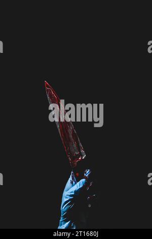 Nach oben zeigende Hand in blauem Handschuh hält blutbeflecktes Messer, dunkler Hintergrund, Halloween, Kopierraum Stockfoto