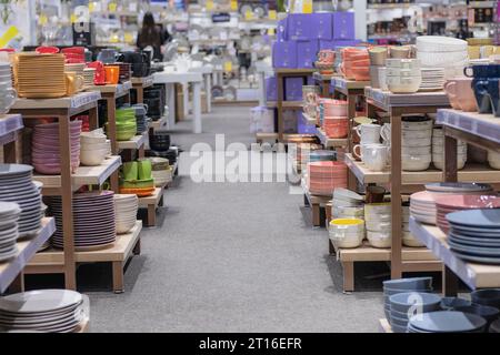 Reihen von verschiedenfarbigen Tassen, Schüsseln und Tellern für Zuhause in Regalen in einem Supermarkt. Das Geschirr wird im Laden verkauft. Stockfoto