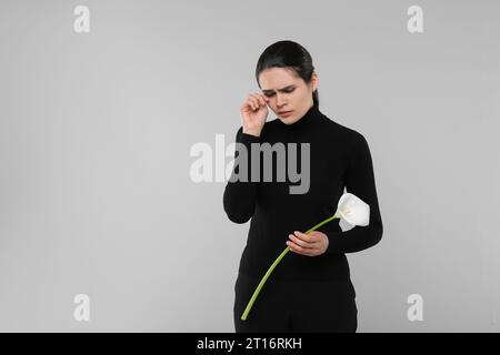 Traurige Frau mit Calla-Lilienblume, die auf hellgrauem Hintergrund trauert, Platz für Text. Trauerfeier Stockfoto