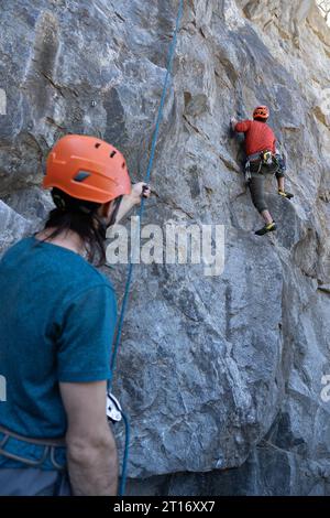 Ein junger Mann versucht, auf einen Felsen zu klettern, während sein Kollege den Sicherheitsgurt hält Stockfoto