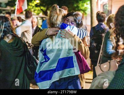 Mainz, Deutschland. Oktober 2023. Eine Frau, die in die israelische Flagge gehüllt ist, nimmt eine andere Frau in die Arme. Die Jüdische Religionsgemeinschaft Mainz-Rheinhessen und die Deutsch-israelische Gesellschaft Mainz haben unter dem Motto "Nein zum Terror, ja zu Israel" zu einer Solidaritätskundgebung aufgerufen. Darlegung: Andreas Arnold/dpa/Alamy Live News Stockfoto