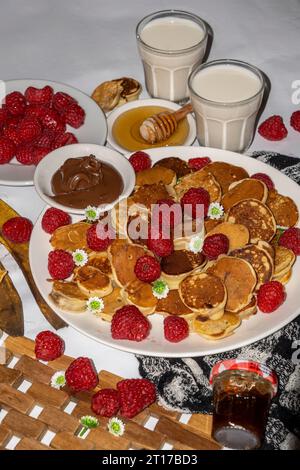 Mini-Pfannkuchen serviert mit Honig, Schokolade, Erdnussbutter und Milch. Fotokonzept für Speisen. Selektive Fokusaufnahme. Stockfoto