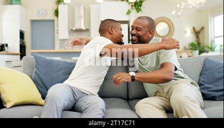 Umarmen, reden und Vater und Sohn auf dem Sofa für einen Besuch, Freundschaft oder Dankbarkeit. Happy, House und ein afrikanischer Vater, der einen erwachsenen Mann zur Begrüßung umschließt Stockfoto