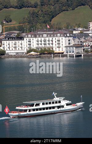 Das Schiff mit dem Namen Brunnen auf dem Vierwaldstättersee bei einer Rundfahrt. Im Hintergrund das Hotel Waldstätterhof in der Ortschaft Brunnen. Hochkant. Das Schiff mit dem Namen Brunnen auf dem Vierwaldstättersee bei einer Rundfahrt. Im Hintergrund das Hotel Waldstätterhof in der Ortschaft Brunnen. Brunnen Kanton Schwyz Schweiz *** das Schiff Brunnen am Vierwaldstättersee bei einer hin- und Rückfahrt im Hintergrund das Hotel Waldstätterhof im Dorf Brunnen aufrecht das Schiff Brunnen am Vierwaldstättersee bei einer hin- und Rückfahrt im Hintergrund das Hotel Waldstätterhof im Dorf Brunne Stockfoto