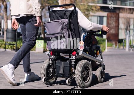 Frau im Rollstuhl mit einem Mann, der spazieren geht Stockfoto