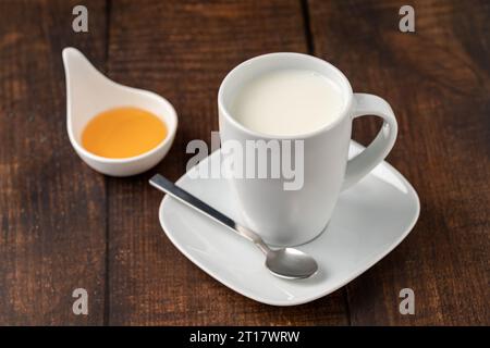 Milch in einer Porzellanschale und Honig in einer Porzellanschale auf einem Holztisch Stockfoto