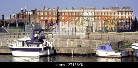 Archival 1997 Blick auf den Hampton Court Palace von der Themse kleine Boote an den Anlegestellen neben Jean Tijou verzierte vergoldete Gittertore und Zaun mit Sir Christopher Wren Gebäude der Südfassade dahinter in Richmond London England Großbritannien Stockfoto