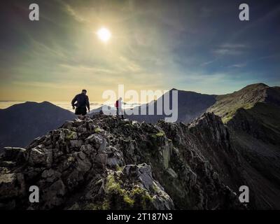 Kletterer auf der anspruchsvollen Crib Goch mit CRI-y-ddysgl und Snowdon in der Ferne und Y Lliwedd an einem sonnigen Herbsttag. Wales. UK. Stockfoto