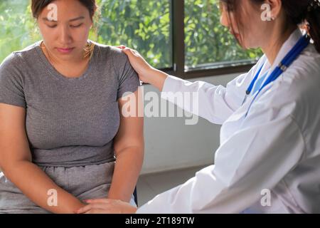 Übergewichtige Frau mit Sprecharzt in der Klinik. Porträt eines freundlich lächelnden Arztes, der Hand auf Schulter hält, den Patienten unterstützt, gibt Stockfoto