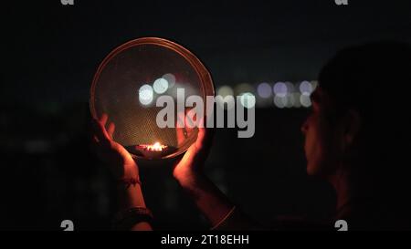 Karva Chauth ist ein eintägiges Festival, das von hinduistischen Frauen für die Sicherheit und Langlebigkeit ihrer Ehemänner gefeiert wird. Indianerin, die durch ein Sieb schaut, ce Stockfoto