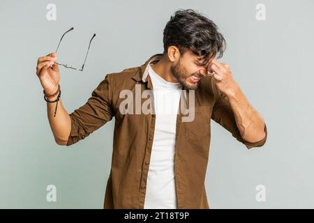 Erschöpfter, müder indischer junger Mann zieht die Brille aus, spürt Augenschmerzen, ist überlastet Burnout von langer Arbeit. Verschlafener, erschöpfter Arabianer, der die Augen isoliert auf grauem Hintergrund reibt Stockfoto