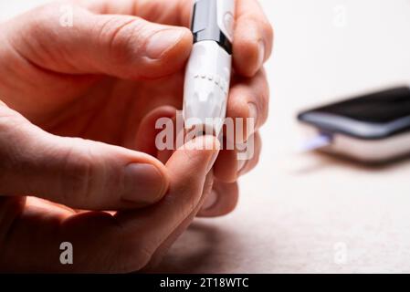 Kaukasischer Mann mittleren Alters hat sich seinen Finger für den Glukosetest zu Hause mit Messgerät und Zubehör im Hintergrund durchbohrt Stockfoto