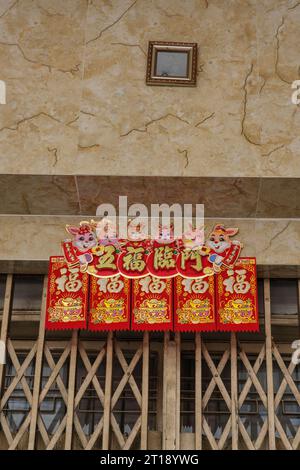 Der kleine Spiegel über der Tür verschreckt Dämonen aus dem Haus. Ho Chi Minh, Vietnam. Ein rot-goldenes Banner verkündet Glück und Glück. Stockfoto