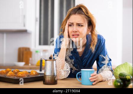 Junge Frau, die an Migräne leidet, Kaffee in der Küche trinkt Stockfoto