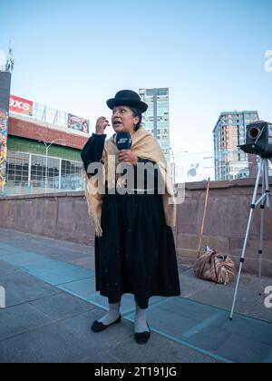 La Paz, Bolivien - 8. August 2022: Bolivianische indigene Frau in traditionellen Trachten steht neben einer Kamera aus Karton und einem Stativ Stockfoto