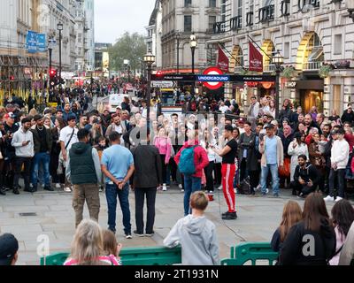 Ein Straßenkünstler unterhält eine Menschenmenge, meist Touristen, im Piccadilly Circus London Stockfoto