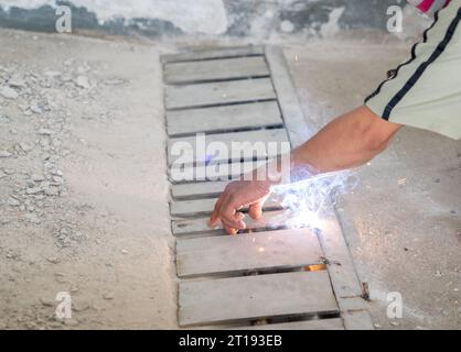 Arbeiter schweißt Edelstahlgitter der Ablaufschiene auf dem Boden. Stockfoto