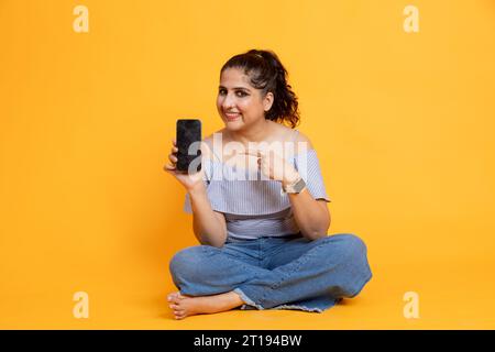 Indische Frau zeigt den Bildschirm des Telefons auf den Bildschirm und zeigt auf das Konzept der mobilen App-Werbung Stockfoto