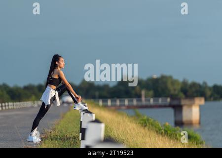 Joggerin, die an einem See steht und ihre Schnürsenkel bindet, Thailand Stockfoto