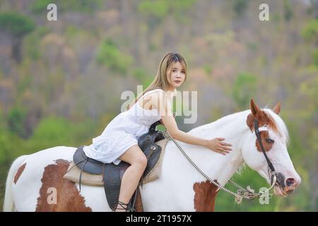 Junge Frau im Sommerkleid, reitet auf einem weißen und braunen Pferd, Thailand Stockfoto