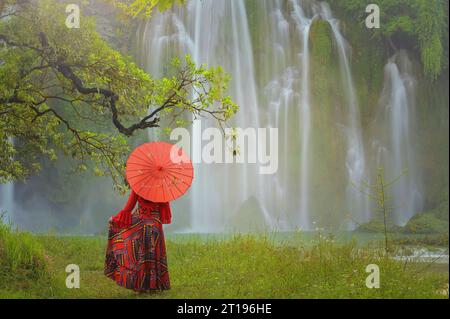 Rückansicht einer Frau mit einem Sonnenschirm, die vor dem Ban Gioc Wasserfall in Cao Bang, Vietnam steht Stockfoto