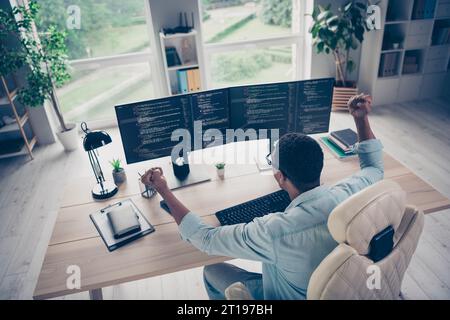 Rückansicht des Lucky Happy Programmierers, der aufsteigende Fäuste auf erfolgreiche IT-Startup-Webdesign-Coder in Innenräumen zu Hause feiert Stockfoto