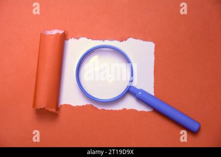 Lupe auf gerissenem rotem Papier. Konzept der Exploration und Analyse. Roter Hintergrund. Kopierbereich. Stockfoto