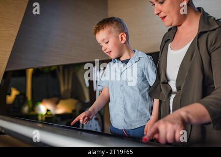 Ein lächelnder kleiner Junge, der sich während eines Museumsbesuchs mit seiner Mutter amüsiert und neugierig interaktive Touchscreen-Displays ansieht. Stockfoto