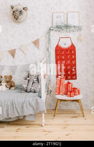 Schöner roter Adventskalender an der Wand im Kinderzimmer mit vielen Spielzeugen, Lichtern und roten Weihnachtsgeschenken Stockfoto