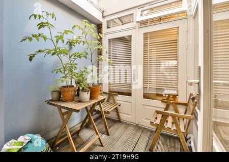 Ein Balkon mit einigen Pflanzen auf dem Tisch und zwei hölzernen Klappstühlen vor der Zimmertür Stockfoto