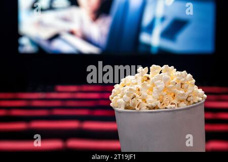 Filme und Popcorn. Popcorn im Kino. Familienfilmnächtekonzept. Action oder romantische Comedy-Unterhaltung auf dem Bildschirm. Dunkles Theater mit roten Sitzen. Stockfoto