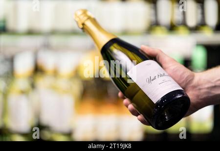 Sekt im Supermarkt oder im Spirituosengeschäft. Mann mit einer Flasche Champagner oder Prosecco im Spirituosenladen. Kunde im Lebensmittelmarkt. Stockfoto