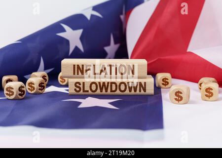 Wirtschafts- und Finanzkonzept. Auf der Flagge der Vereinigten Staaten liegen Würfel mit dem Dollarsymbol und Holzsterben mit der Aufschrift Inflation Slowdo Stockfoto