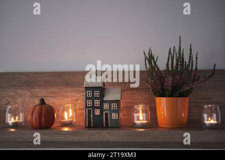 Niedliches Herbstarrangement für Hygge-Wohnkultur. Dekoratives Haus, Kerzen, Heidekraut und Kürbis. Stockfoto