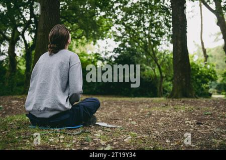 Rückansicht einer Frau, die in einem Wald sitzt Stockfoto