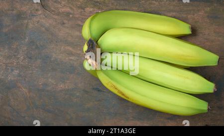 Frische Bananen auf einem Holztisch, geerntete tropische Früchte auf rustikalem Hintergrund, direkt von oben mit selektivem Fokus und Kopie aufgenommen Stockfoto